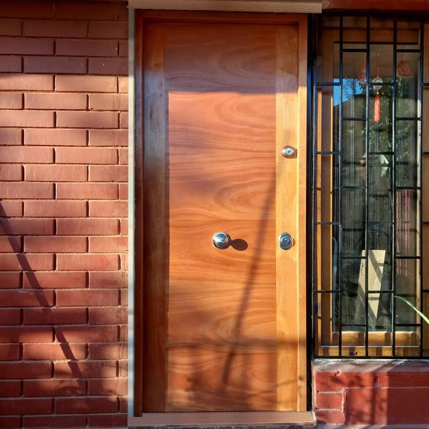 Puerta blindada de madera terminada, instalada por America Project en una casa de ladrillo en Santiago
