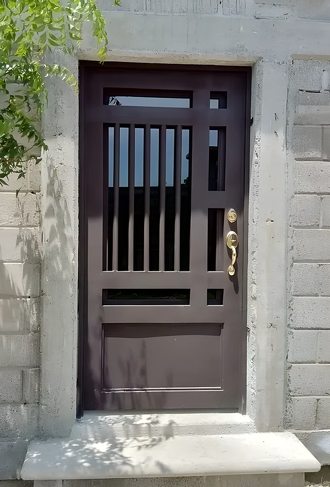 Puerta de seguridad modelo Managua, de acero café oscuro con rejería vertical en la parte superior y manilla dorada